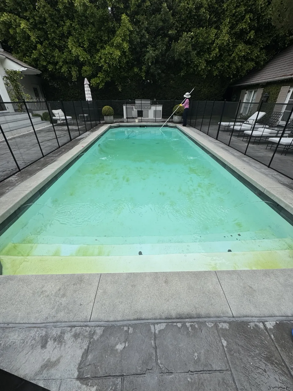 Rectangular fenced pool with debris and green areas visible on the shallow steps